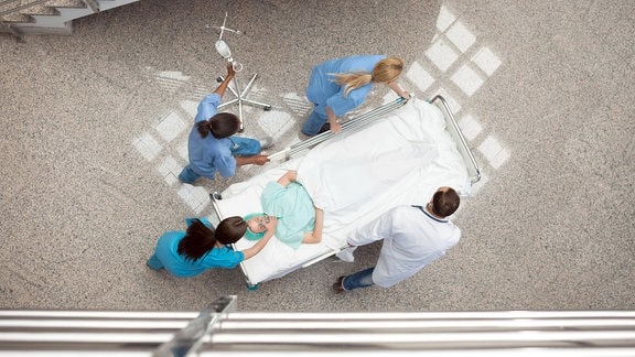 Drei Krankenschwestern und ein Arzt schieben einen Patienten in einem Bett im Krankenhausflur.