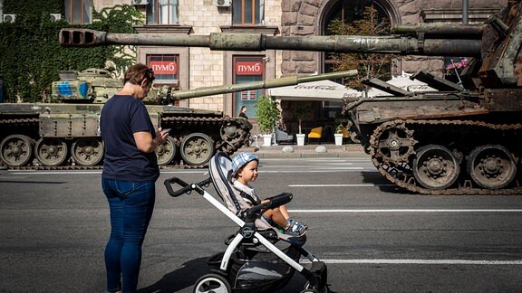 Mutter mit Kinderwagen macht Fotos von zerstörten russischen Panzern