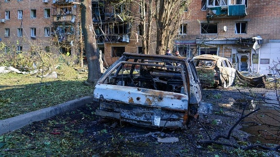 Autowracks stehen vor einer zerstörten Hausfassade.