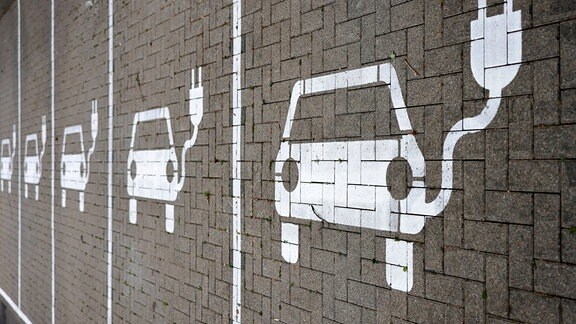 Piktogramme mit Autos, aus denen ein Stromkabel ragt, markieren Parkplätze mit Ladesäulen.