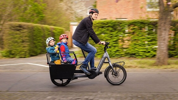 Ein Mann fährt zwei Kinder mit dem Lastenrad