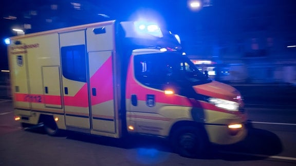Ein Rettungswagen fährt mit Blaulicht nachts durch eine Stadt.