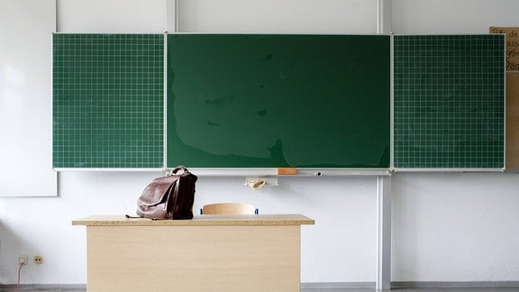 Eine Tasche steht auf einem Pult vor einer Tafel.