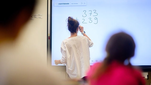Ein Lehrerin schreibt eine Mathematikaufgabe auf eine digitale Schultafel im Klassenraum einer 4. Klasse einer Grundschule in der Region Hannover.