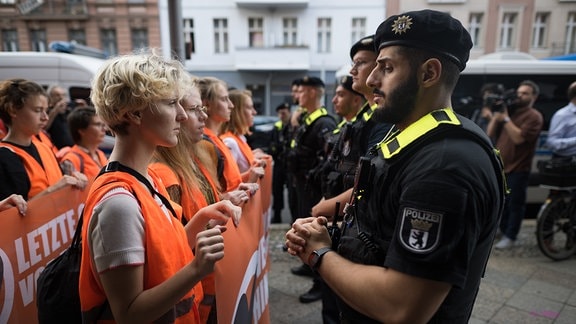 Polizeibeamte stehen zu Beginn eines Protestmarsches der Klimaschutzgruppe Letzte Generation vor Teilnehmern der Demonstration.
