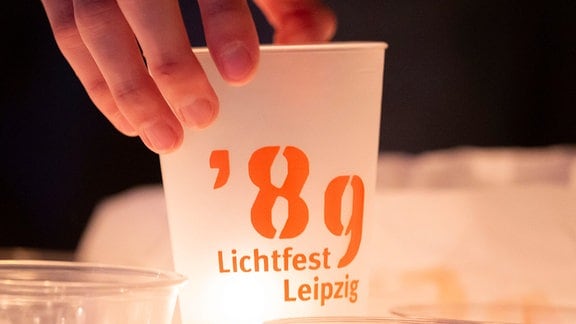 Eine Kerze lässt einen Becher mit der Aufschrift „'89 Lichtfest Leipzig“ im Hof der Nikolaikirche in Lepzig leuchten. 