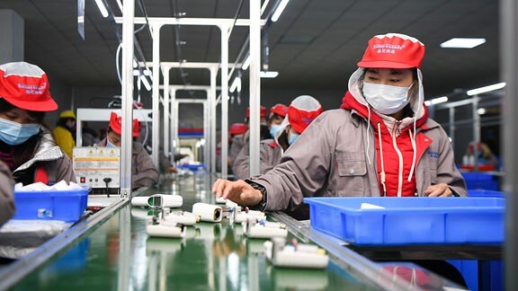 Menschen arbeiten in einer Fabrik am Fließband.