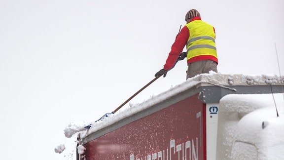 Ein Mann befreit das Dach eines eingeschneiten LKW vom Schnee.