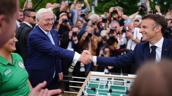 Emmanuel Macron und Frank-Walter Steinmeier stehen beim Demokratiefest aus Anlass von 75 Jahren Grundgesetz an einem Tischkicker. 