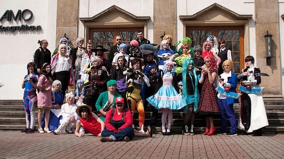 Kostümierte Manga-Fans posieren auf einer Treppe stehend vor dem Messegebäude