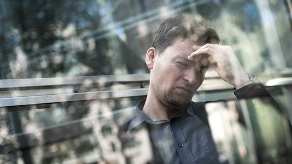 Ein Mann steht in einem Bürogebäude  im Fahrstuhl und fasst sich gestresst an die Stirn.