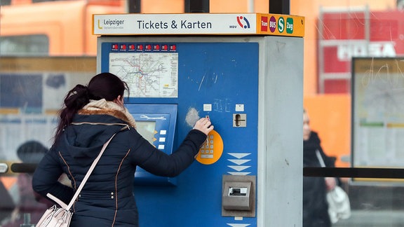 Eine Frau kauft an einer Haltestelle an einem Automaten eine Fahrkarte für die Straßenbahn