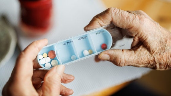 Eine über 90-jährige Dame nimmt eine mit Medikamenten gefüllte Tablettenbox mit Fächern für die Tageszeiten morgens, mittags, abends und nachts aus einem Wochendispenser.