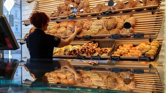 Eine Mitarbeiterin räumt Mischbrot in die Auslage einer Bäckerei.