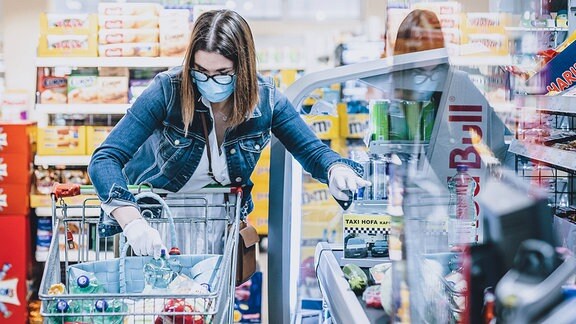 Eine Frau trägt eine Schutzmaske und Handschuhe bei ihrem Einkauf in einem Supermarkt. 