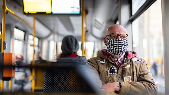 Ein Mann sitzt auf dem Weg zur Arbeit in einer Straßenbahn und trägt einen Mundschutz.