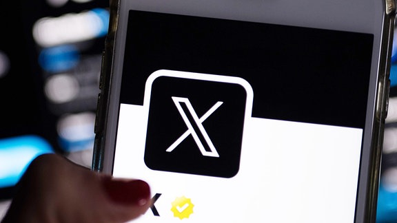 Auf dem offiziellen Profil der Plattform X auf dem Bildschirm eines Smartphones ist der weiße Buchstabe X auf schwarzem Hintergrund zu sehen.