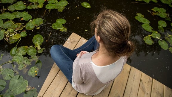 Eine junge Frau sitzt auf einem Steg und meditiert