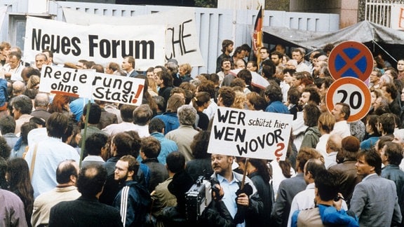 Demonstranten stehen vor der besetzten Stasi-Zentrale in Ost-Berlin mit Bannern und Transparenten. "Neues Forum" oder "Regierung ohne Stasi" ist darauf zu lesen. 