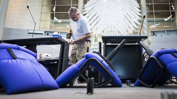 Handwerker schraubt Tische und Stühle in den Plenarsaal des Bundestags