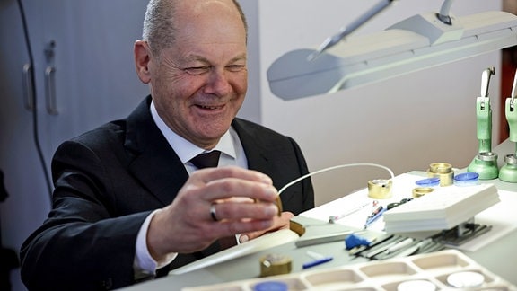 Bundeskanzler Olaf Scholz betrachtet ein Werkstück in der Produktionsstätte des deutschen Uhrenherstellers Nomos Glashütte