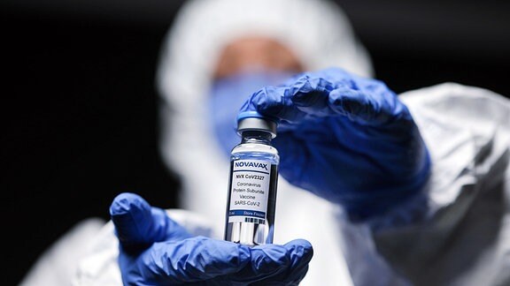 Person Schutzkleidung präsentiert eine Ampulle Novavax-Impfstoff