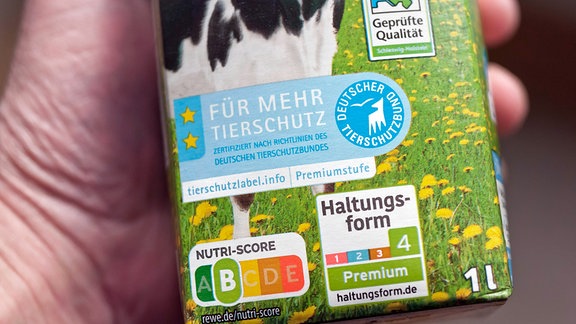 Eine Hand hält eine Packung Weidemilch auf der mehrere unterschiedliche Kennzeichnungen aufgedruckt sind.ds