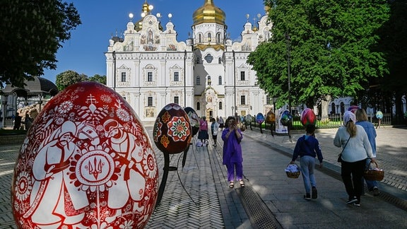Menschen gehen mit Osterkörben neben dekorativen Ostereiern zur Mariä-Entschlafens-Kathedrale von Kiew-Pechersk Lawra.