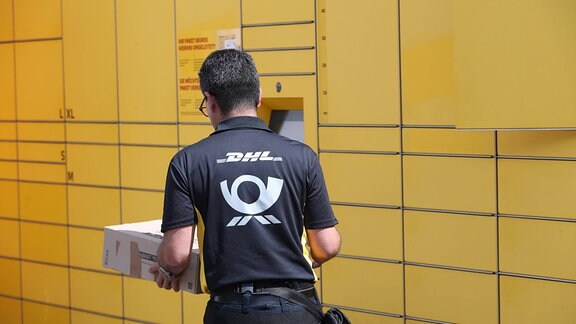 Ein Postbote der Deutschen Post entnimmt Pakete aus eine DHL Packstation.