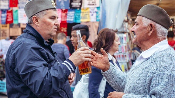 Zwei Männer auf einem Markt in Serbien, einer mit einer Flasche in der Hand