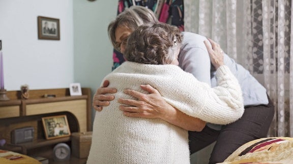 Eine Frau hilft ihrer 93-jährigen Mutter beim Aufstehen und Ankleiden.