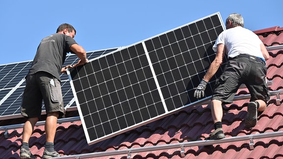 Zwei Handwerker montieren eine Photovoltaik-Anlage auf einem roten Ziegeldach