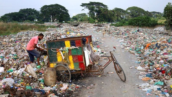 Ein Mann neben einem Fahrrad inmitten von Müll durch den ein Pfad führt
