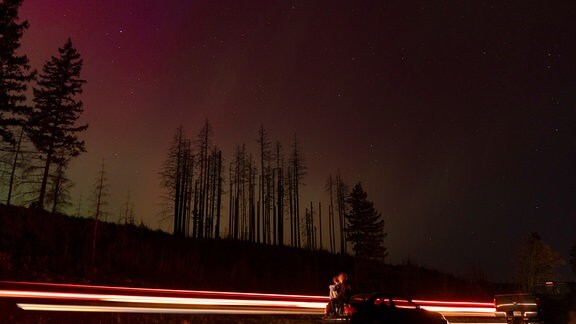 Autos fahren vorbei, während Menschen in den Nachthimmel schauen, um das Nordlicht (Aurora Borealis) zu sehen (Langzeitbelichtung).