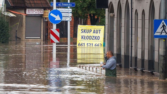 Ein Mann steht in hüfthohem Wasser, das nach tagelangem, ungewöhnlich starkem Regen die Straßen und Häuser überflutet hat. 