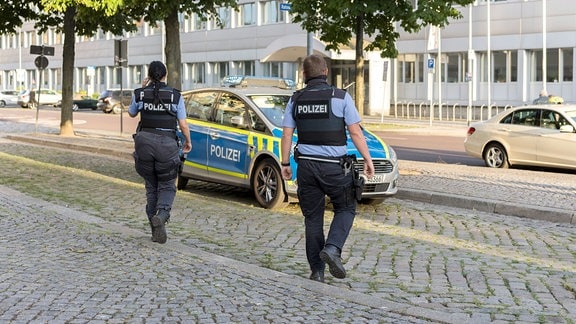 2 Polizeibeamte gehen zum Streifenwagen in Magdeburg.