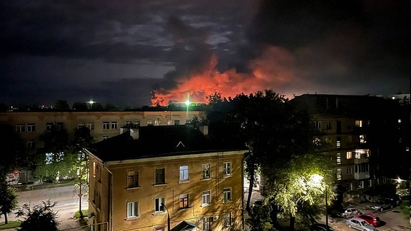 Eine rote Qualmwolke steigt am Horizont hinter Gebäuden auf.