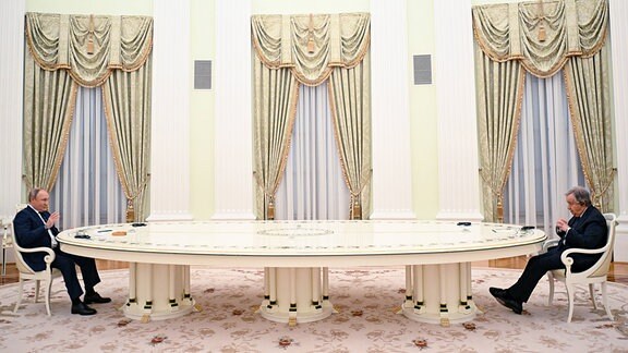 Vladimir Putin (l) und Antonio Guterres (r) sitzen mit viel Abstand an einem ovalen Tisch.