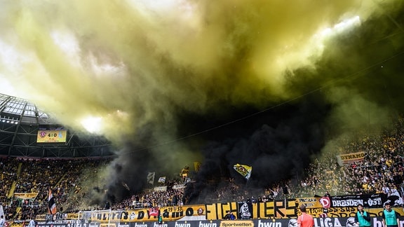 Eine Rauchwolke schwebt über Fans im Stadion.