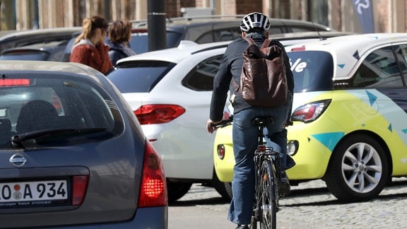 Ein Fahrradfahrer fährt hinter parkenden Autos entlang. 