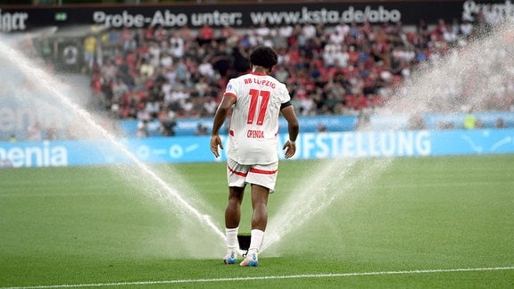 Lois Openda, RB Leipzig, läuft durch die Wasserfontainen des Rasenbewässerung.