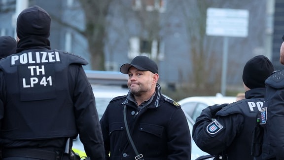 Versammlungsanmelder Christian Klar steht zwischen Polizeibeamten bei einer Demonstration gegen eine geplante Erstaufnahmeeinrichtung für Flüchtlinge im ehemaligen Wismut Krankenhaus. 