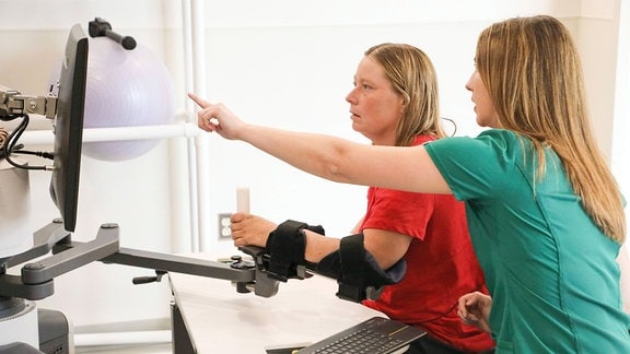 Shannon Watkins, 42, in der Mitte, benutzt den InMotion ARM von BIONIK Labs für die neurologische Rehabilitation, während sie mit der Ergotherapeutin Samantha Rubio, rechts, arbeitet.