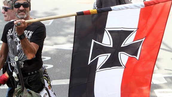 Ein Mann trägt eine schwarz weiß rote Reichskriegsflagge des Deutschen Reiches.