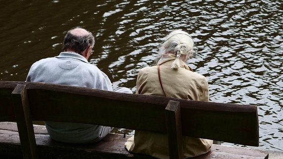 Ein älteres Paar sitzt im Bremer Blockland an der Wuemme auf einer Bank am Wasser.