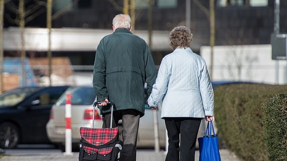 Ein älteres Paar geht händchenhaltend über die Straße.