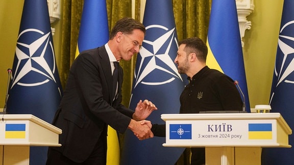 NATO-Generalsekretär Mark Rutte (l) und der ukrainische Präsident Wolodymyr Selenskyj geben sich während einer Pressekonferenz die Hand.