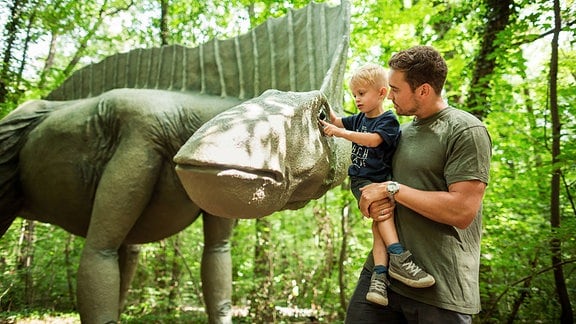 Vater mit Kind neben einem Saurier im Saurierpark