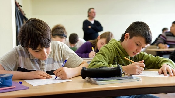 Ein Lehrer beaufsichtigt eine Schulklasse während einer schriftlichen Leistungskontrolle.