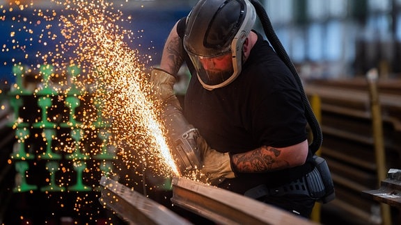 Ein Arbeiter bearbeitet ein Eisenteil mit einem Winkelschleifer.